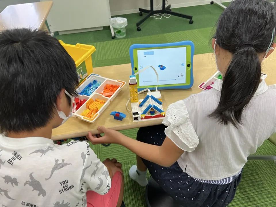 姫路の子ども向けSTEAM|英語で学ぶものづくり|ワンダーランド 3 タブレットを見ながら、一緒にブロックを組み立てる子どもたち
