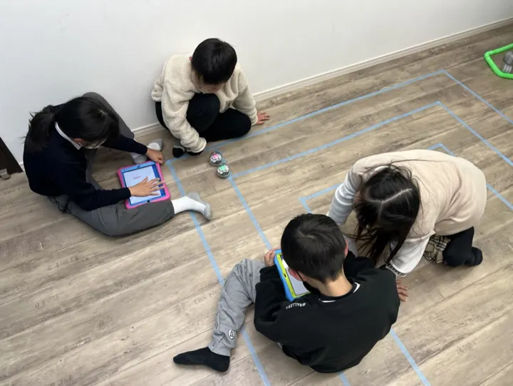 姫路の子ども向けSTEAM|英語で学ぶものづくり|ワンダーランド 6 床のコースで小さなロボットとタブレットを使う子どもたち